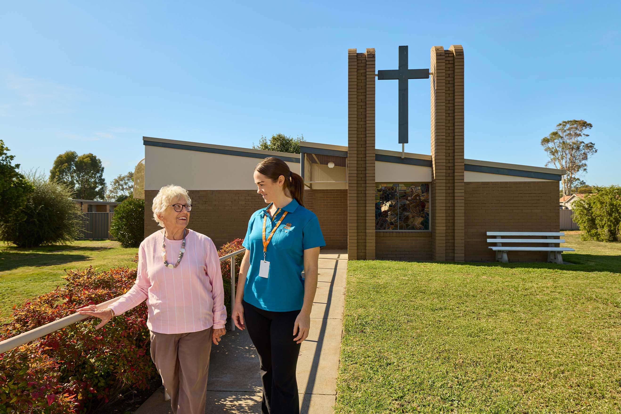 Resident and Benetas team member walking together outside the chapel at Benetas Eaglehawk