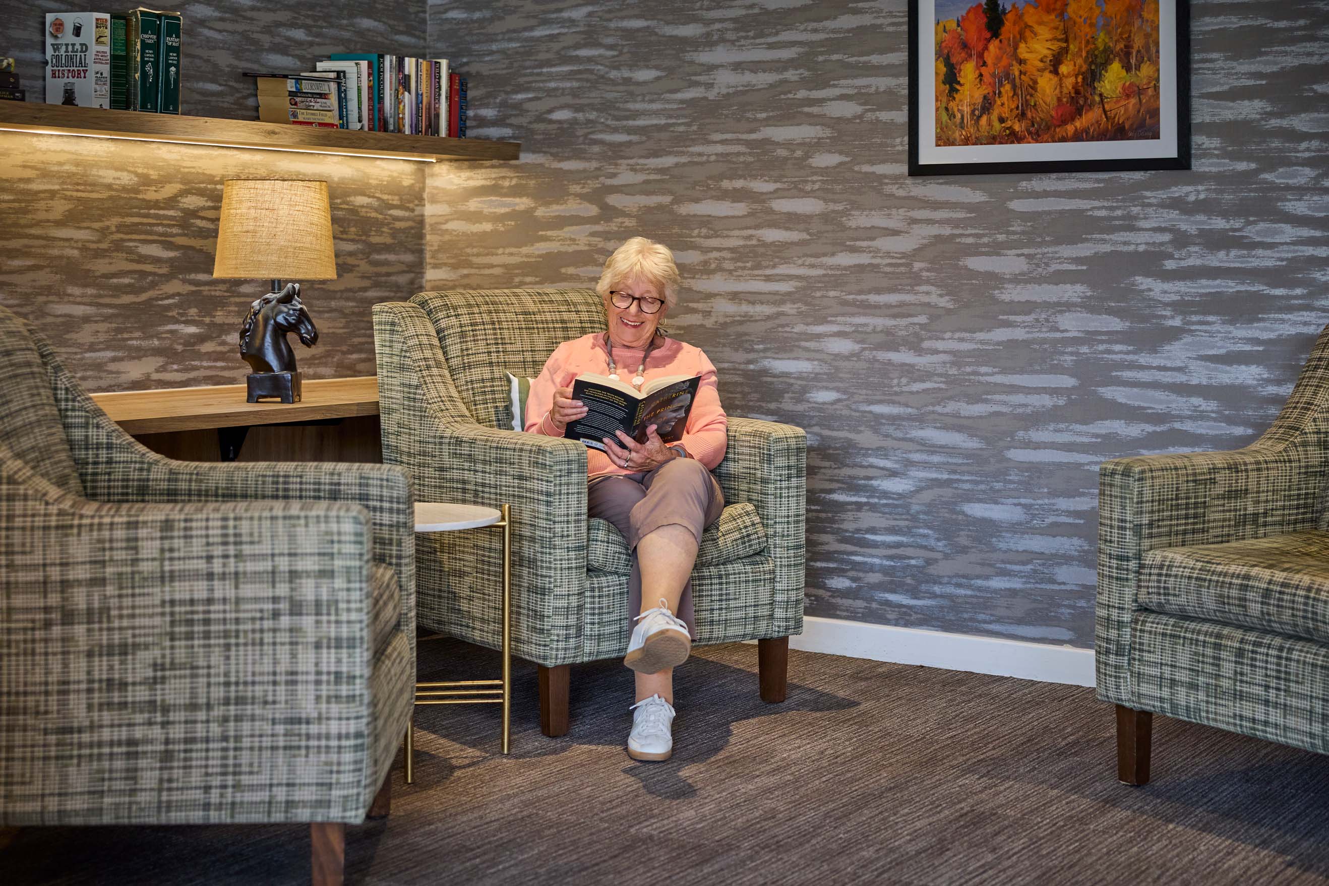 Resident reading a book in a comfortable library sitting area at Benetas Eaglehawk