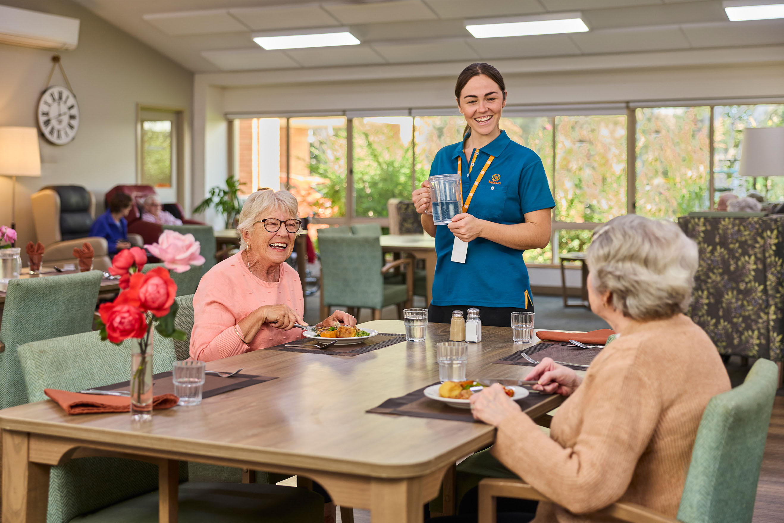 Residents enjoying a meal with support from a Benetas team member in the dining room at Benetas Kangaroo Flat