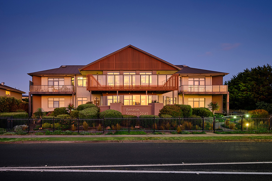 The welcoming exterior of Benetas Corowa Court, showcasing a beautifully landscaped entrance at dusk with warm lights illuminating the building