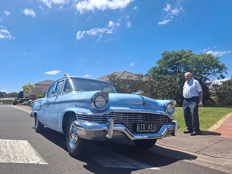 A man poses next to a vintage car, highlighting its classic features and the nostalgic charm of the automobile.
