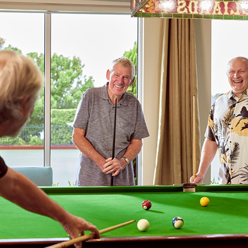 Three older men playing pool in a dimly lit room, focusing on their precise shots and intense concentration.